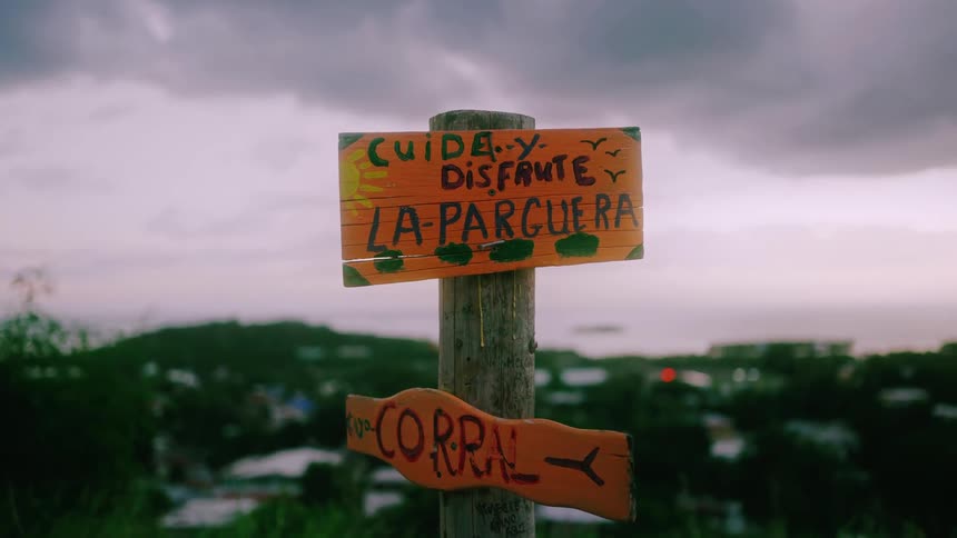 Close up of a rustic wooden sign against the backdrop of a city in the mountains by the sea on a cloudy day