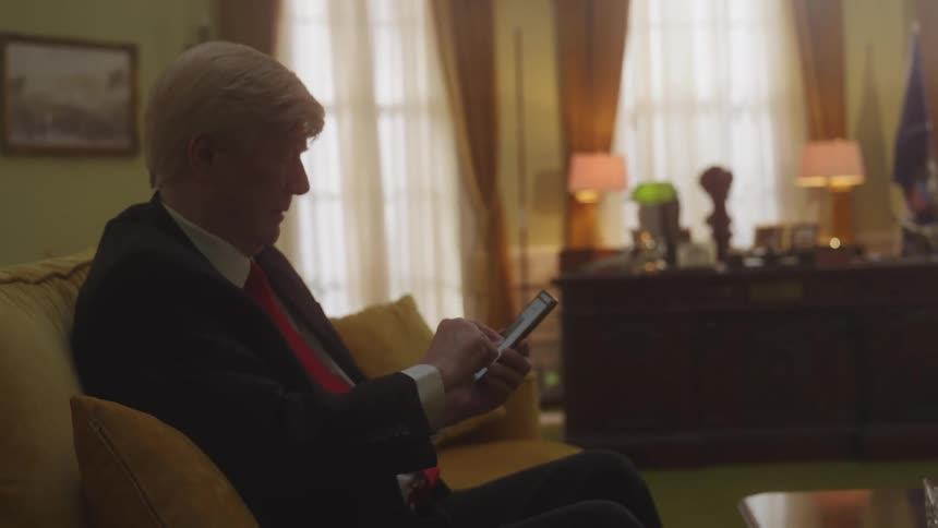An elderly man is scrolling on his phone as he sits on a couch