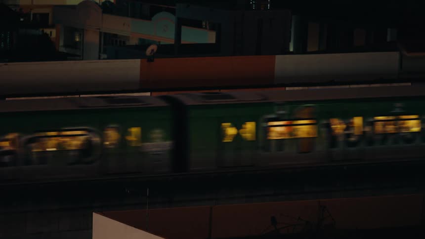 A train passing through a train station without stopping with its interior lights reflecting outward due to the nighttime setting