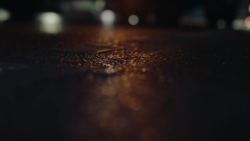A wet city street at night with blurred car headlights reflecting on the asphalt as a vehicle speeds past