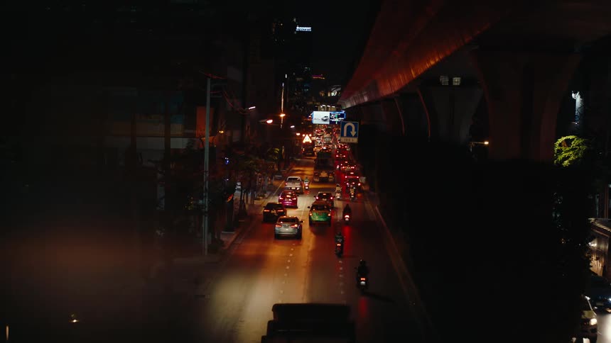 Traffic flows down a city street under an overpass at night