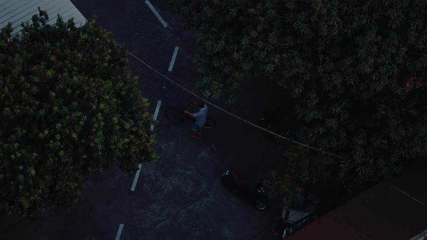 A man taking his bicycle which is parked next to a motorcycle beside a tree in his backyard as he gets ready to ride it during the day