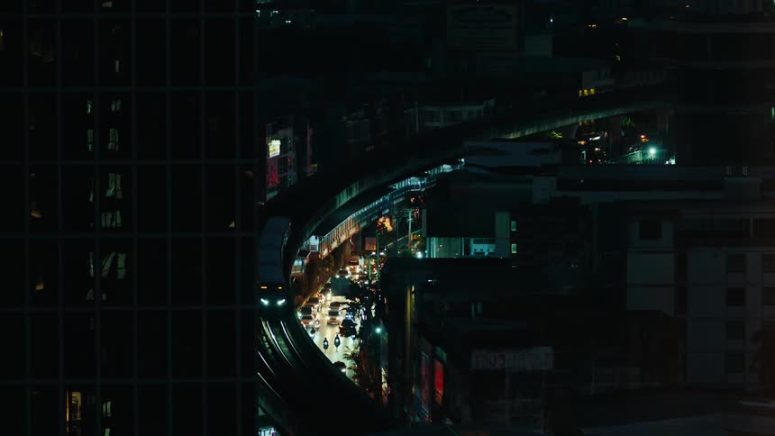 A train rides in a circle above a street full of cars and lights downtown at night