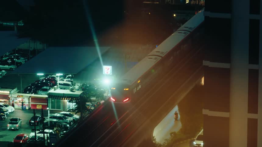 A train drives by on an overpass above a gas station at night