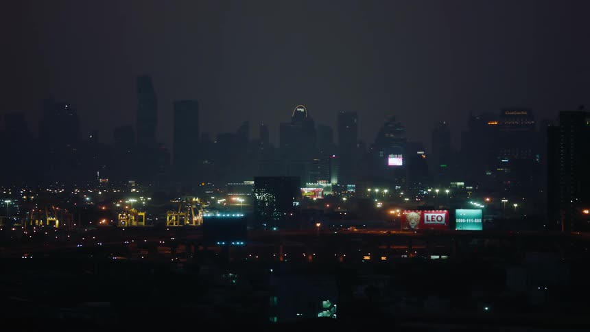 Traffic driving along a highway passes a foggy city skyline at night