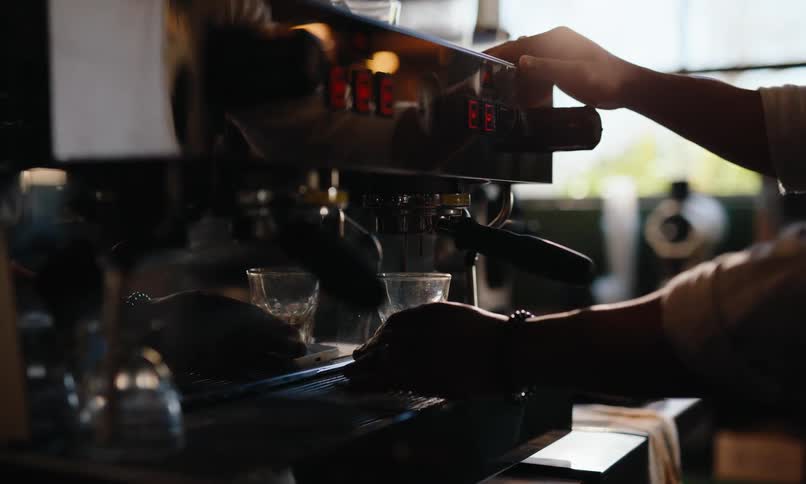 Female worker fills a glass using a machine at a coffee shop