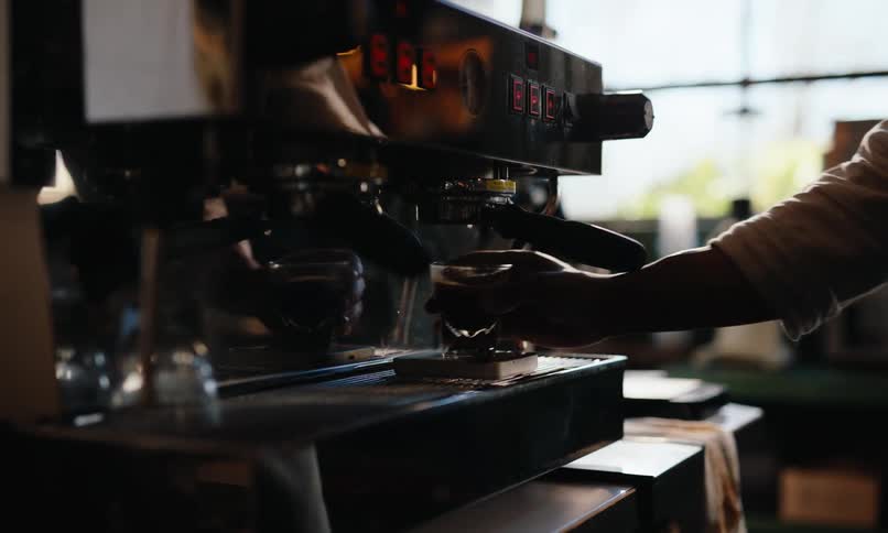 A person grabs a cup from an espresso machine in a restaurant