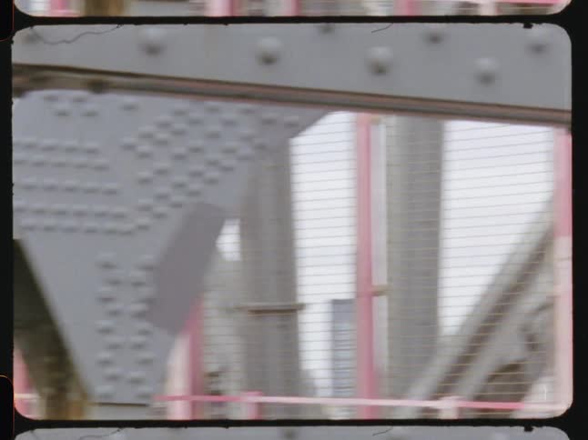 A bridge with protective railings and metal pillars and in the background there is a city of economic buildings