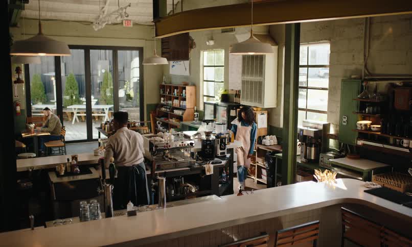 Customers sitting at a table in a coffee shop with two waiters in aprons