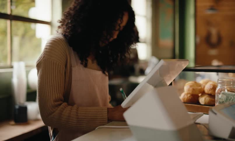 A woman takes notes from a tablet behind a counter and a man wipes the counter