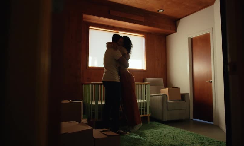 A couple is looking at a crib then they hug each other
