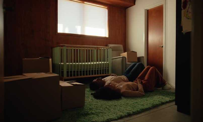 A man and a woman are lying on the floor of a room with a wooden crib and are talking happily