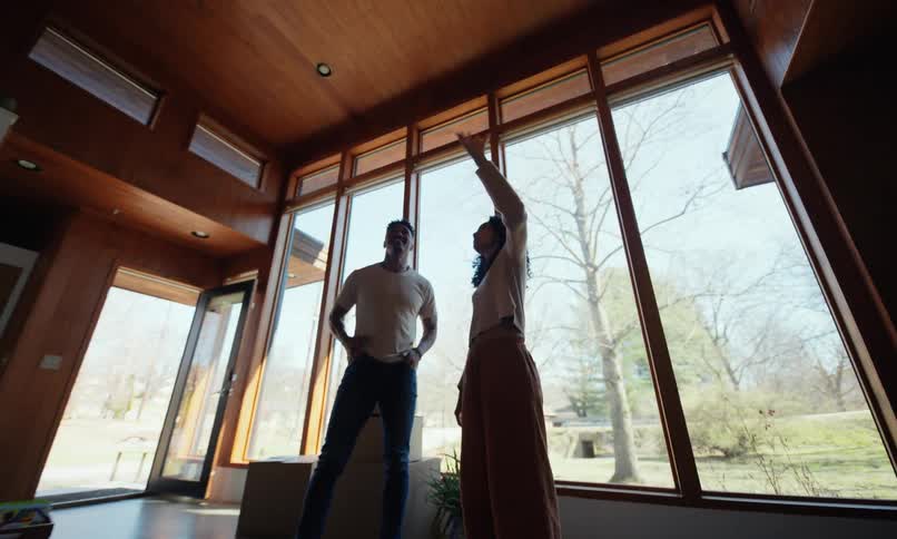 A couple point around an empty room with boxes