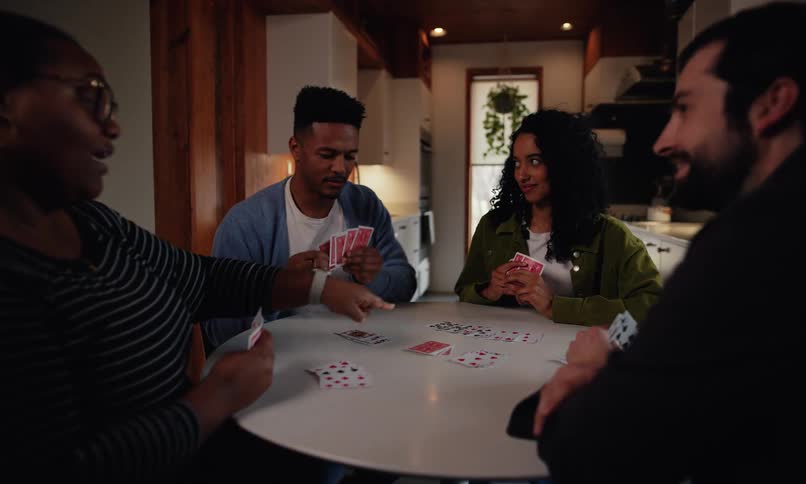 Friends sit at a round table playing cards