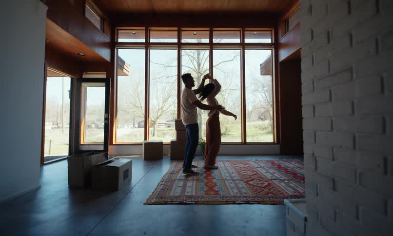 A couple dances in their new living room surrounded by boxes