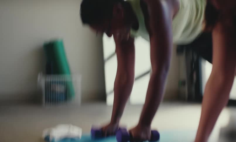 Two women lifting hand weights in a plank position on yoga mats