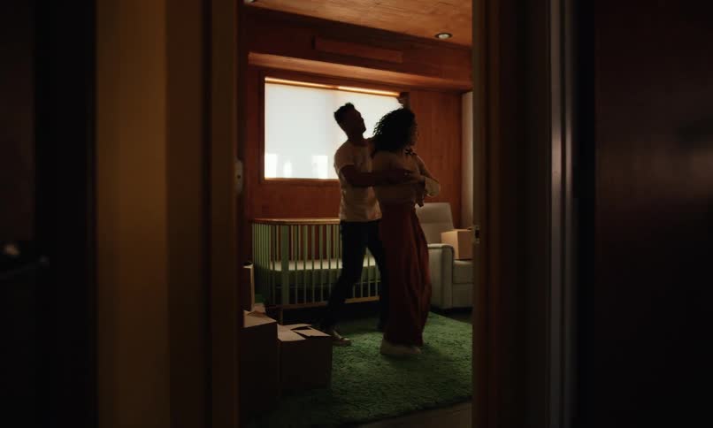 A couple dances by a crib in a room with boxes