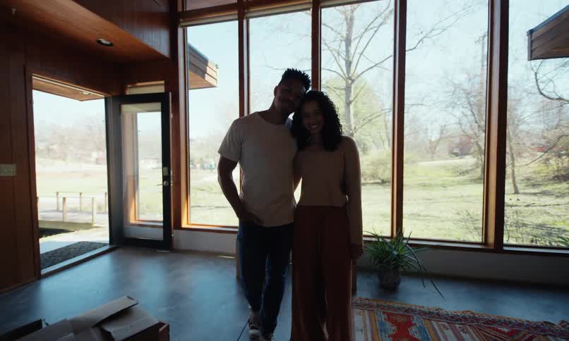 Couple smiles while leaning together in the living room of their new home on a sunny autumn day