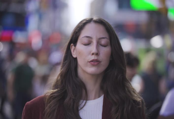 Woman keeps her eyes closed and takes a deep breath with a large crowd of people passing by in the city