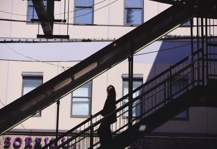 A silhouetted figure walks down an outdoor staircase in front of a building