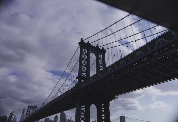 Cars drive under the manhattan bridge in new york city on a mostly cloudy day