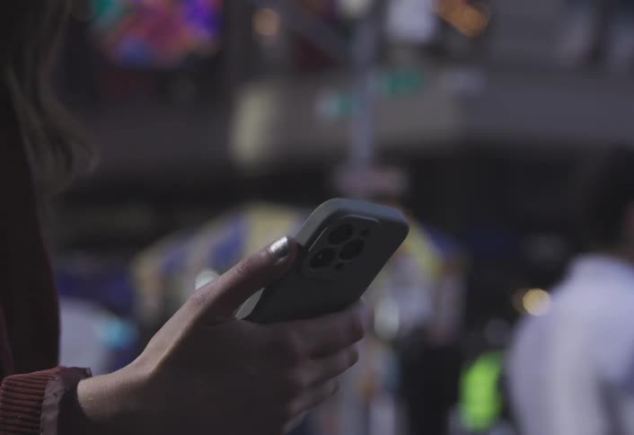 A person is texting on their phone as other people walk past in a city