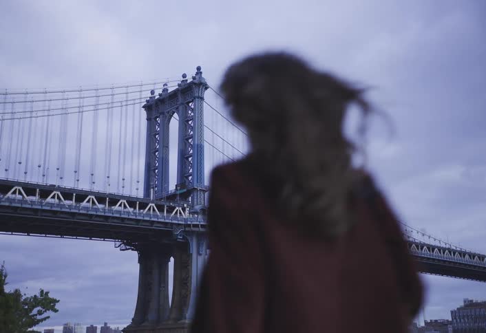 Woman walking past the manhattan bridge on a cloudy day