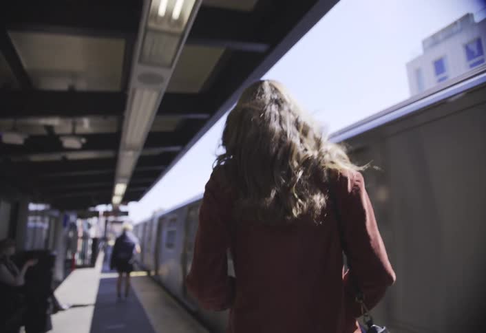 Back shot of a woman walking on a train platform as a train passes by