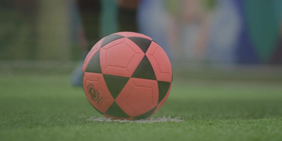 Person kicking an orange soccer ball with black details positioned on artificial grass