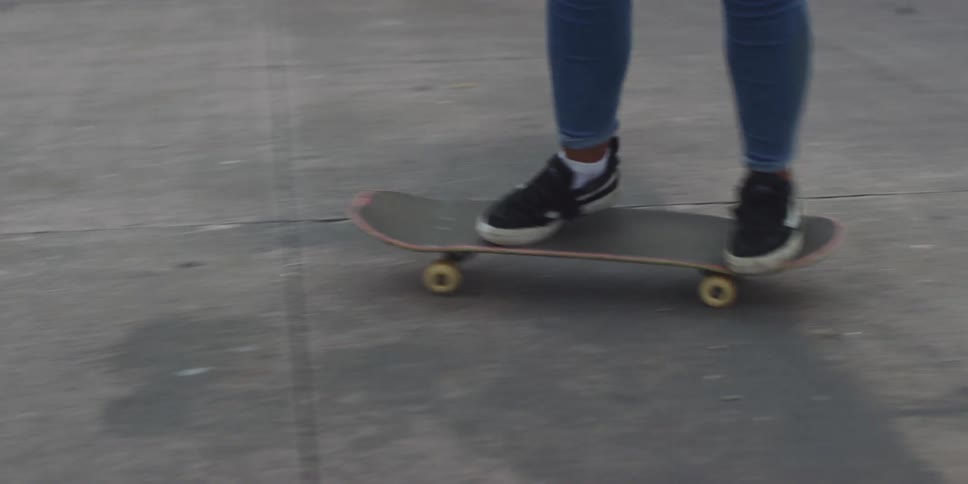 A teenage girl wearing jeans is riding a skateboard on a city sidewalk