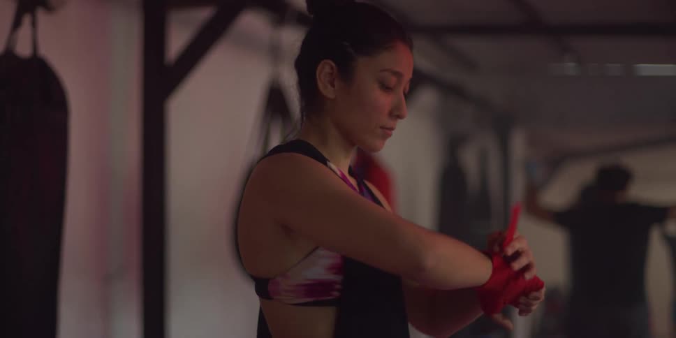 Woman puts on workout gloves as people do jumping jacks behind her in a gym