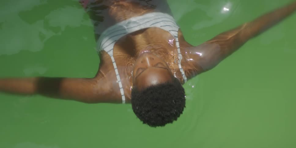 A black teenage girl wearing a swimsuit is swimming in a pool at midday