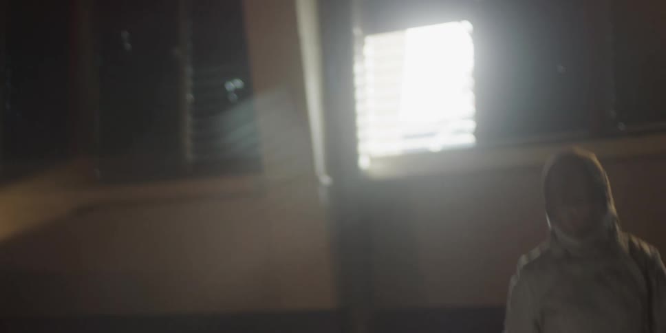 A fencer in protective gear lunges forward gripping a sword with sunlight streaming through a nearby window