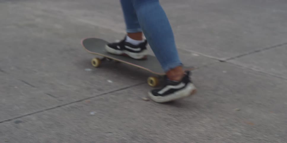 A skateboarder in blackandwhite sneakers and blue jeans performs a skateboard flip trick landing smoothly and continuing to skate