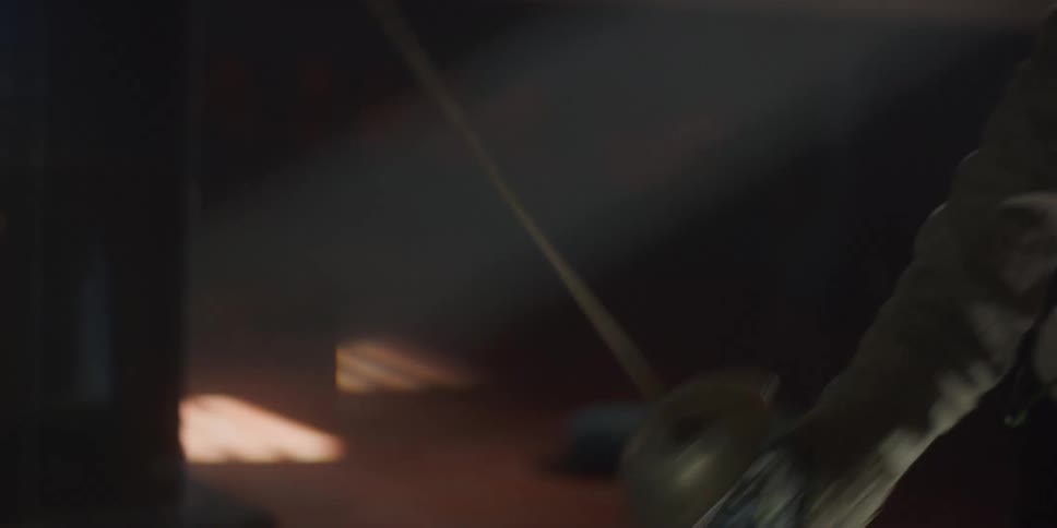 Two individuals are engaged in fencing within a dimly lit gym with one lunging forward and the other preparing to block