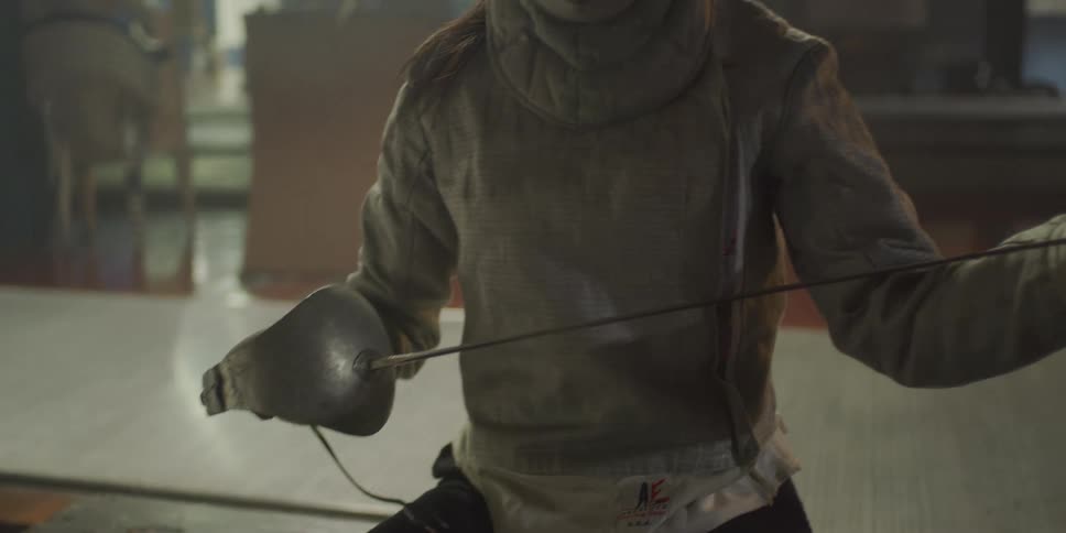 Person sitting holding a fencing sword in protective clothing