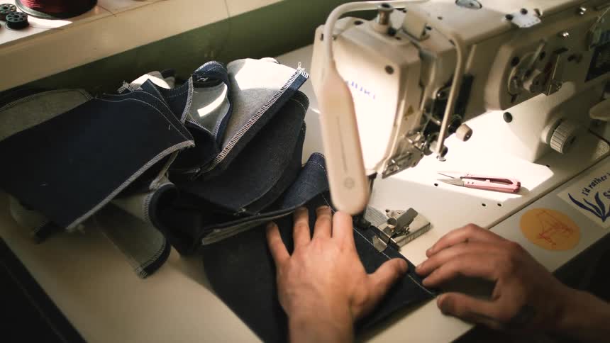 A man sews dark denim pockets with a sewing machine