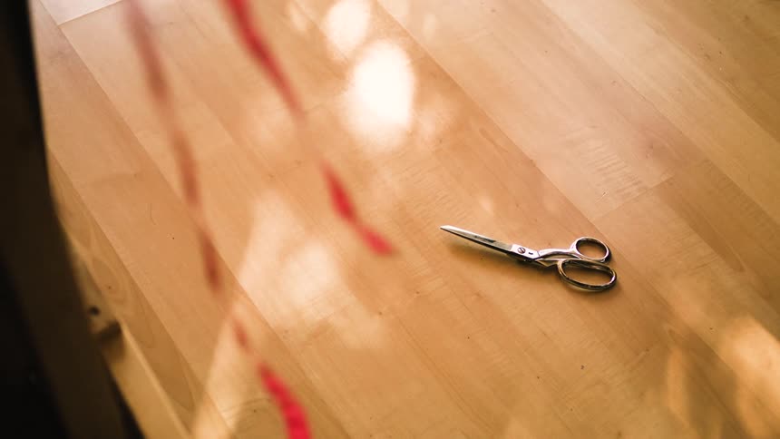 Red ribbon in the foreground and in the background a pair of scissors on a wooden bench