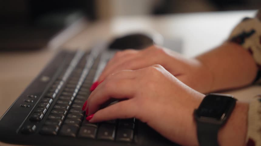 A woman is at a desk typing on a computer keyboard