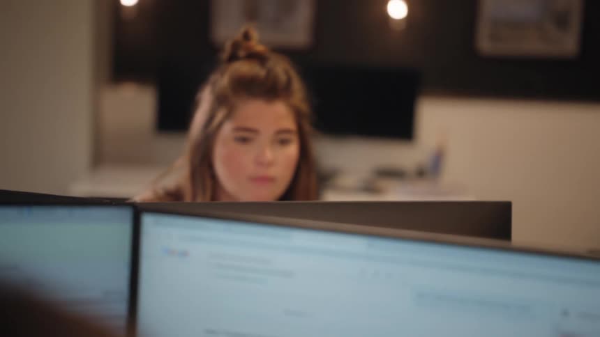 A female employee stares at dual monitors in an office environment
