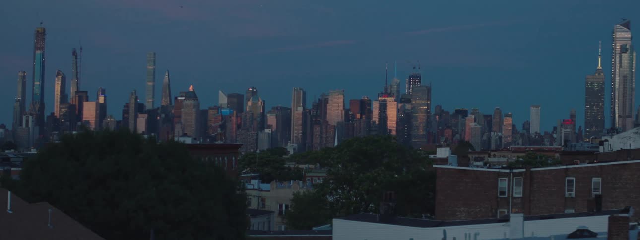 A city skyline viewed from a residential neighborhood with a series of skyscrapers visible in the distance at sunrise
