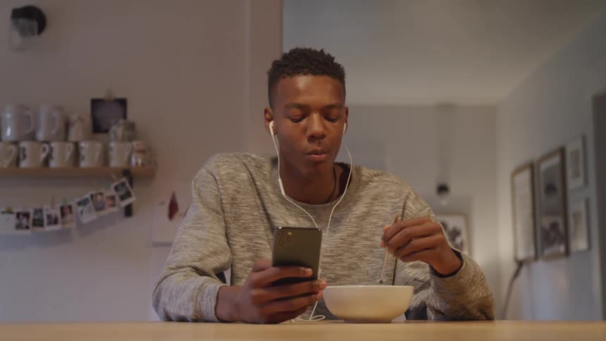 A guy eats cereal while on his phone