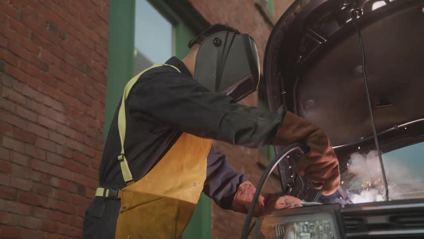 Mechanic wearing protective clothing and mask welding a vehicle engine