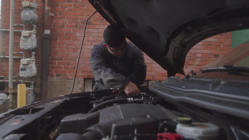 Concentrated mechanic performing repairs on a car engine with the hood open