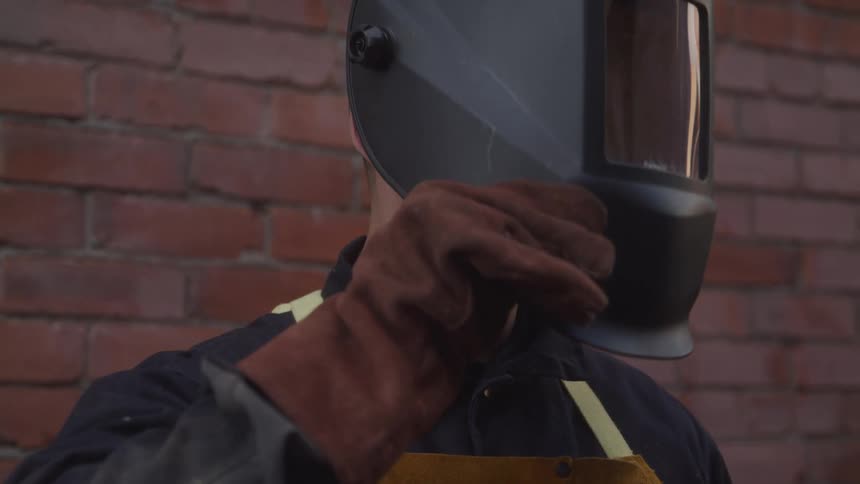 Man lowering welding mask with one gloved hand