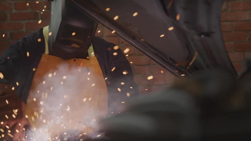 Mechanic with protective mask welding a vehicle engine with sparks coming out