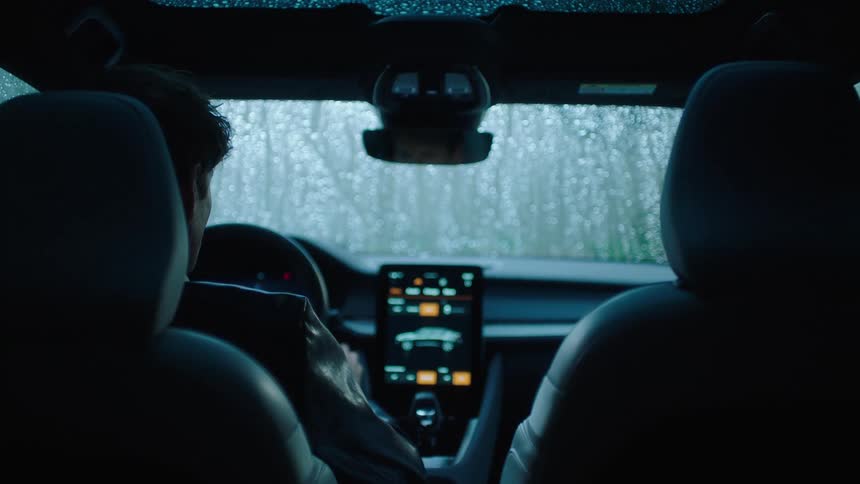A man sitting in the front seat of a car where there is multimedia with a drawing of the vehicle and raindrops falling on the windshield