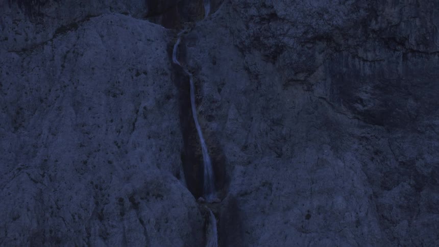 A stream flows between cracks in a rocky terrain at sunrise with soft light casting a warm glow over the landscape