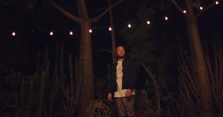 Man in an outdoor setting at night with warm lighting and trees around