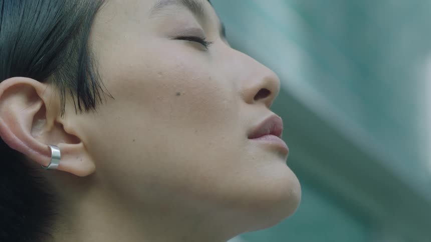 Closeup profile of an asian woman outdoors wearing an earring with her eyes closed and face tilted upward